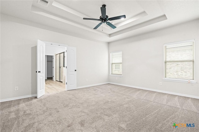 carpeted empty room with ceiling fan and a tray ceiling