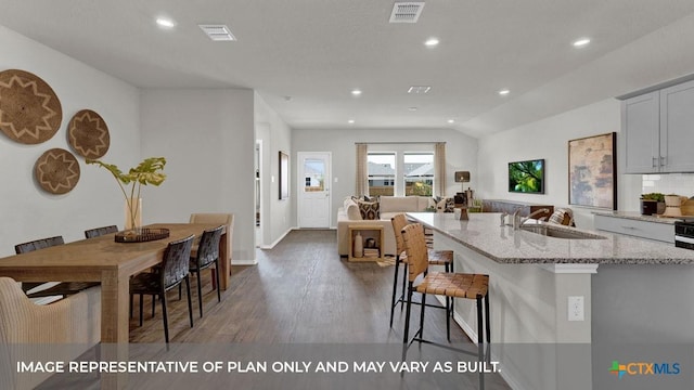 kitchen featuring a kitchen breakfast bar, light stone counters, gray cabinetry, sink, and a center island with sink