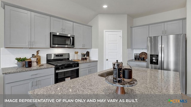 kitchen featuring tasteful backsplash, light stone countertops, lofted ceiling, and appliances with stainless steel finishes