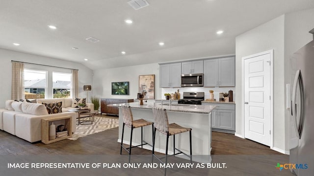 kitchen featuring gray cabinetry, a center island with sink, vaulted ceiling, light stone counters, and stainless steel appliances