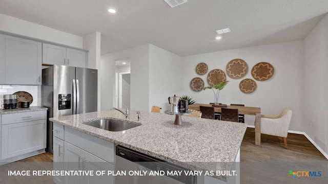 kitchen with sink, hardwood / wood-style flooring, light stone countertops, an island with sink, and appliances with stainless steel finishes