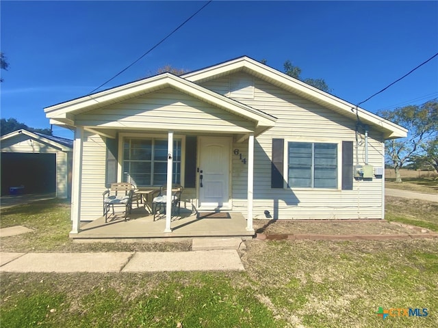 bungalow featuring covered porch, a front lawn, an outbuilding, and a garage