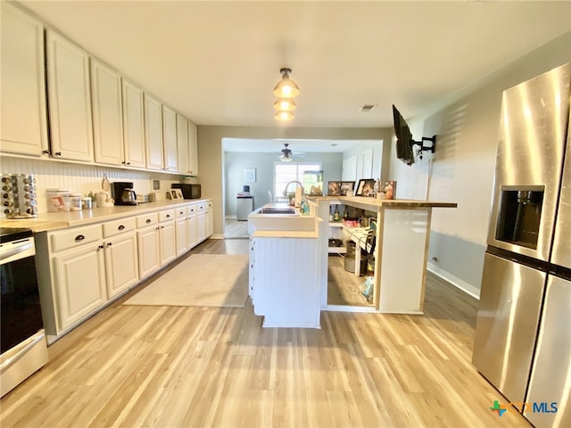 kitchen featuring stainless steel fridge, sink, white cabinetry, range with electric cooktop, and a center island with sink