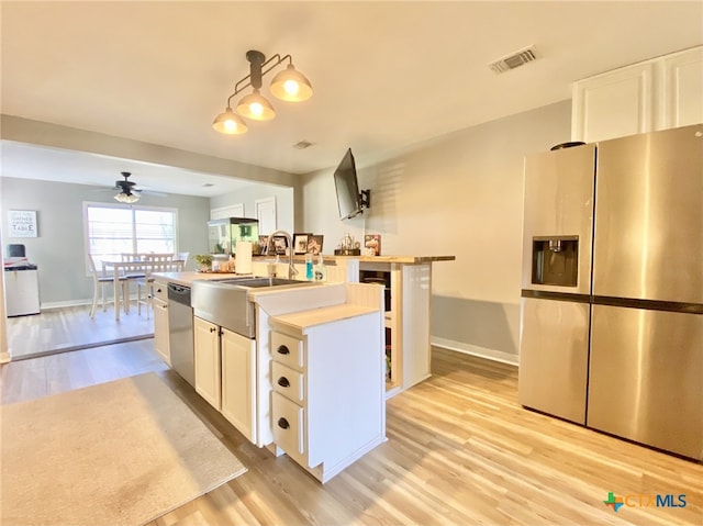 kitchen with decorative light fixtures, white cabinetry, stainless steel appliances, light hardwood / wood-style floors, and a center island with sink