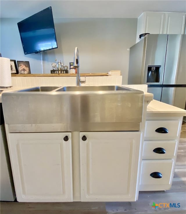 kitchen with stainless steel refrigerator with ice dispenser, sink, white cabinetry, and hardwood / wood-style flooring