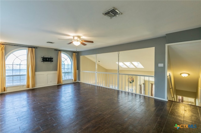 unfurnished room featuring lofted ceiling with skylight, ceiling fan, and dark hardwood / wood-style floors