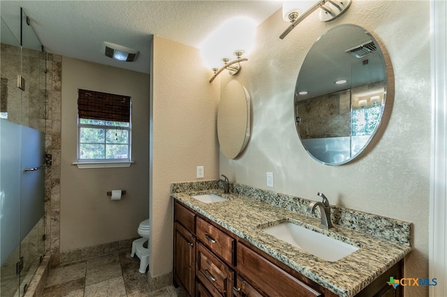 bathroom with tiled shower, vanity, a textured ceiling, and toilet