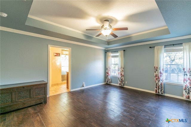 empty room with dark wood-type flooring, ceiling fan, a raised ceiling, and crown molding