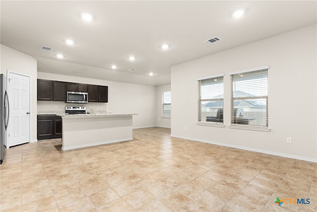 kitchen featuring light tile patterned floors, an island with sink, dark brown cabinets, light stone counters, and stainless steel appliances