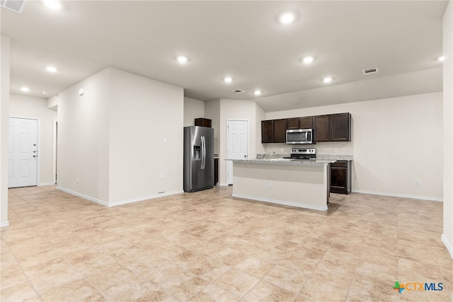 kitchen featuring light stone counters, dark brown cabinetry, an island with sink, and appliances with stainless steel finishes