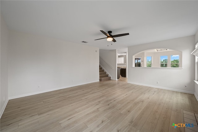 907 Pecos Cv, Leander, TX 78641 - unfurnished living room with a ceiling fan, light wood finished floors, baseboards, stairway, and arched walkways