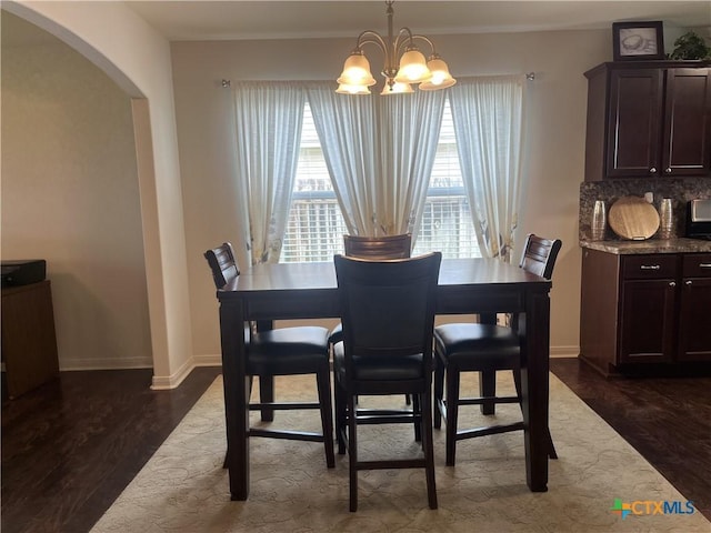 906 2nd St, Cuero, TX 77954 - dining area featuring arched walkways, a chandelier, dark wood-type flooring, and baseboards