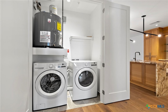 laundry area featuring electric water heater, sink, washer and clothes dryer, and light hardwood / wood-style flooring