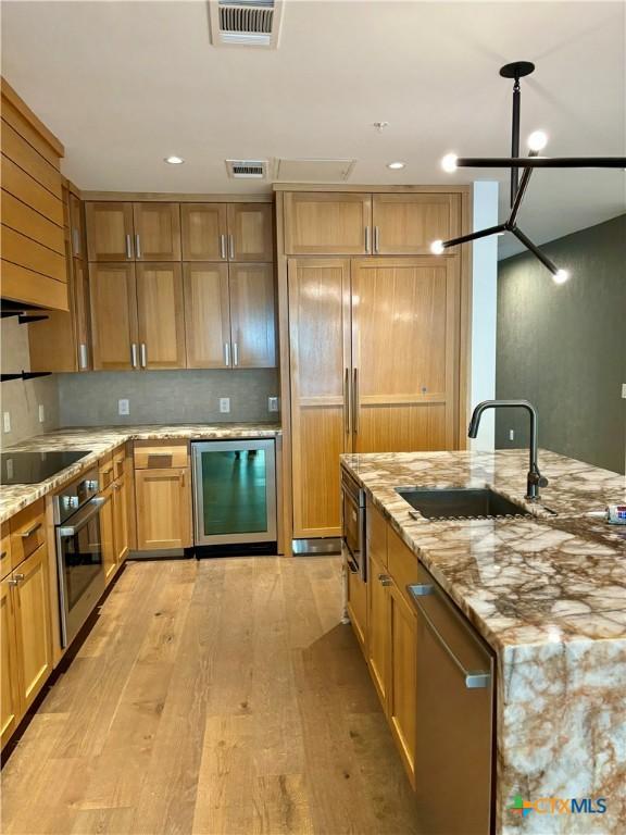 kitchen with light stone countertops, appliances with stainless steel finishes, beverage cooler, sink, and light hardwood / wood-style flooring