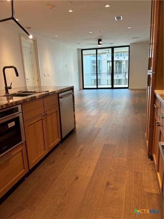 kitchen featuring ceiling fan, sink, expansive windows, hardwood / wood-style floors, and appliances with stainless steel finishes