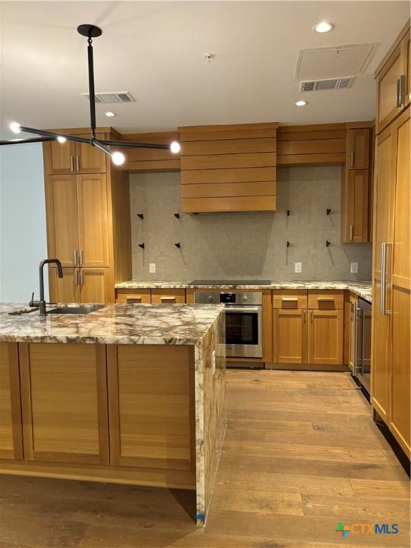 kitchen featuring oven, sink, decorative backsplash, light stone countertops, and light wood-type flooring