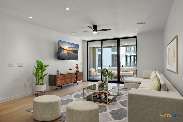 living room featuring ceiling fan, a wall of windows, and light hardwood / wood-style flooring