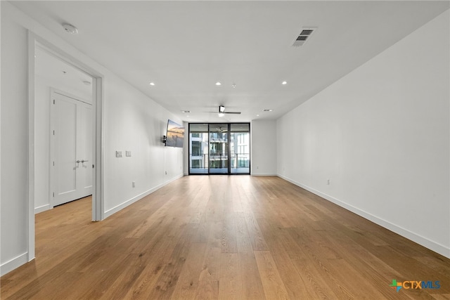 empty room with a wall of windows, ceiling fan, and light hardwood / wood-style flooring