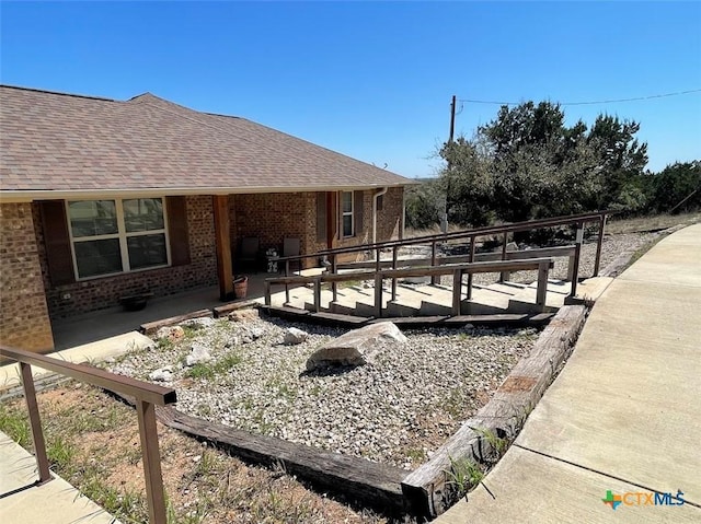 exterior space with a deck, brick siding, and a shingled roof