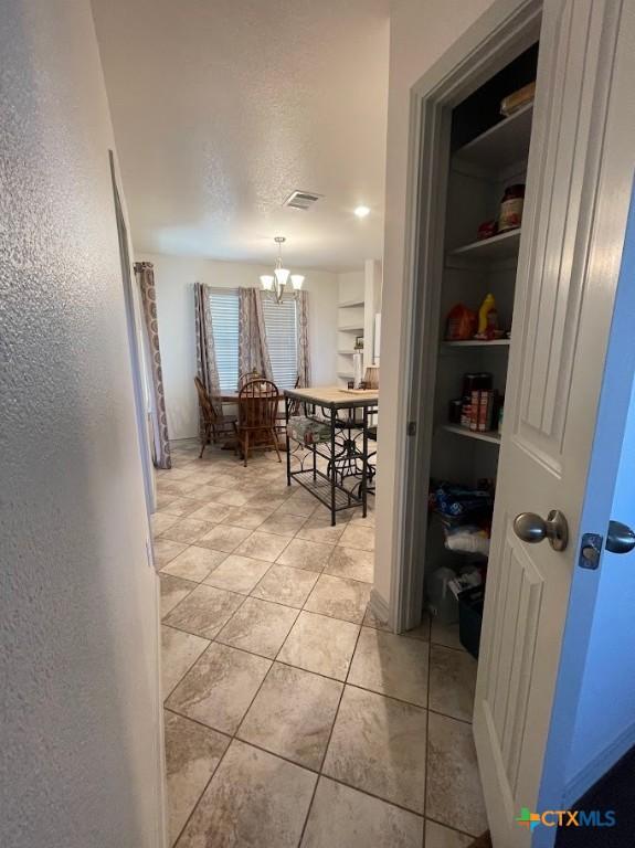 corridor featuring visible vents, a textured ceiling, light tile patterned flooring, a chandelier, and a textured wall