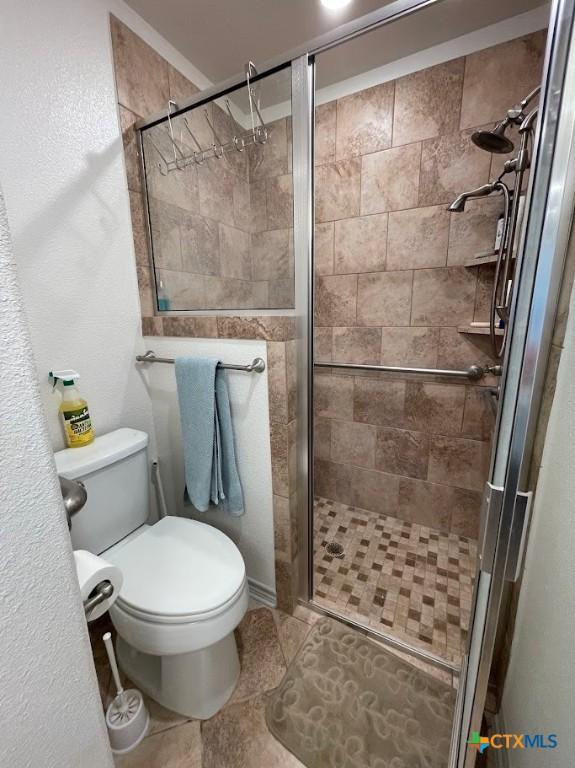 full bath featuring tile patterned floors, toilet, and a stall shower