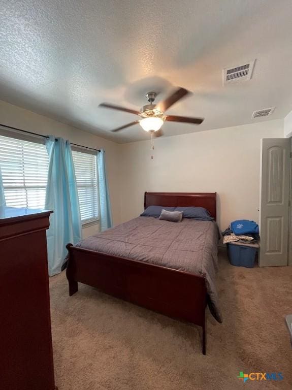 bedroom featuring ceiling fan, a textured ceiling, visible vents, and light carpet