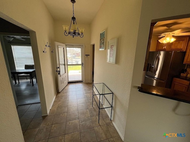 entrance foyer with baseboards, dark tile patterned flooring, and ceiling fan with notable chandelier