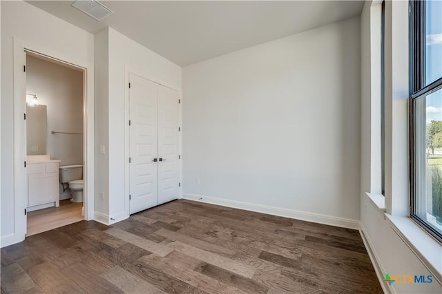 unfurnished bedroom with ensuite bathroom and dark hardwood / wood-style floors