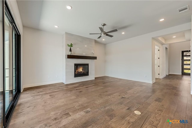 unfurnished living room with hardwood / wood-style flooring, ceiling fan, and a tiled fireplace