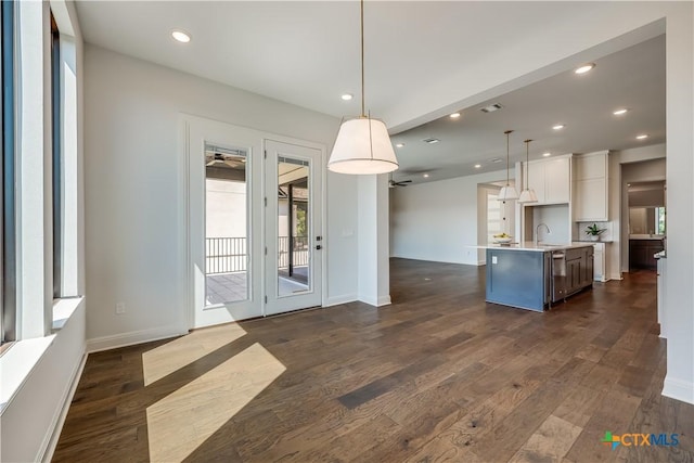 kitchen featuring dark hardwood / wood-style flooring, white cabinetry, an island with sink, and hanging light fixtures