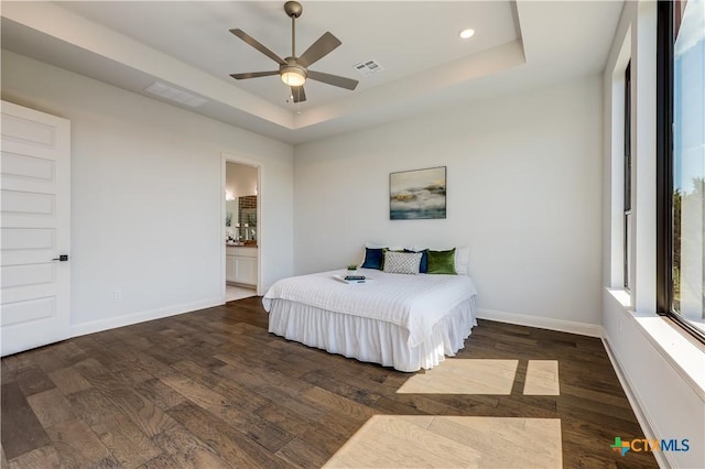 bedroom featuring a raised ceiling, ceiling fan, dark wood-type flooring, and ensuite bathroom