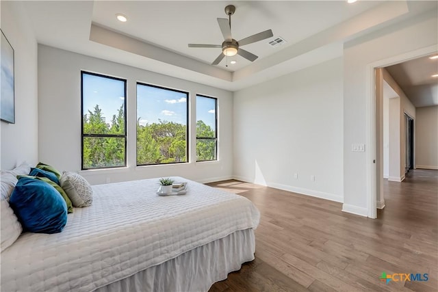 bedroom with wood-type flooring, a tray ceiling, and ceiling fan