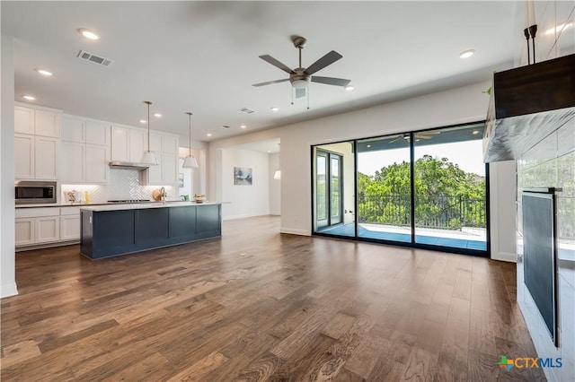 kitchen featuring white cabinetry, stainless steel microwave, dark wood-type flooring, pendant lighting, and a kitchen island with sink