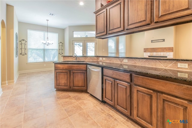 kitchen with dark stone counters, a notable chandelier, hanging light fixtures, sink, and stainless steel dishwasher