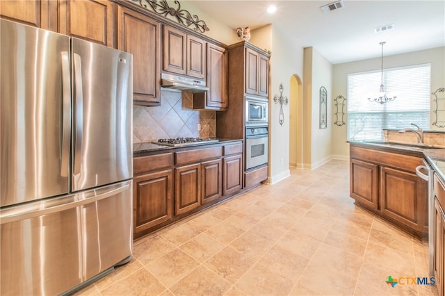 kitchen featuring dark stone counters, an inviting chandelier, sink, backsplash, and appliances with stainless steel finishes