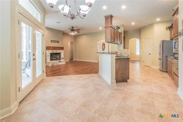 kitchen featuring stainless steel appliances, plenty of natural light, a fireplace, and ceiling fan with notable chandelier