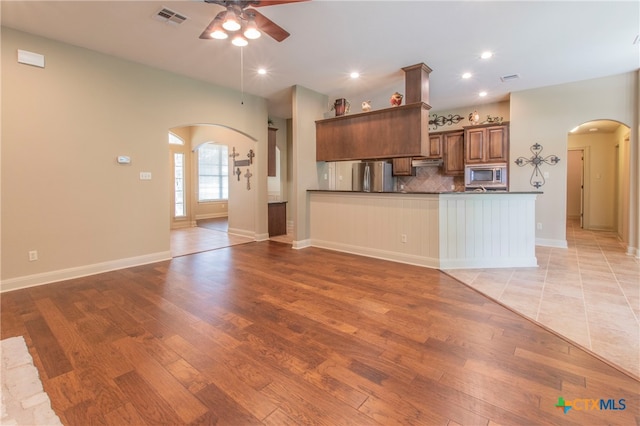 kitchen featuring kitchen peninsula, ceiling fan, backsplash, light wood-type flooring, and appliances with stainless steel finishes