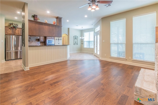 unfurnished living room with ceiling fan with notable chandelier and light hardwood / wood-style floors