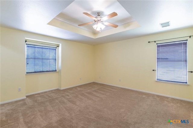 carpeted empty room with ceiling fan, ornamental molding, and a raised ceiling