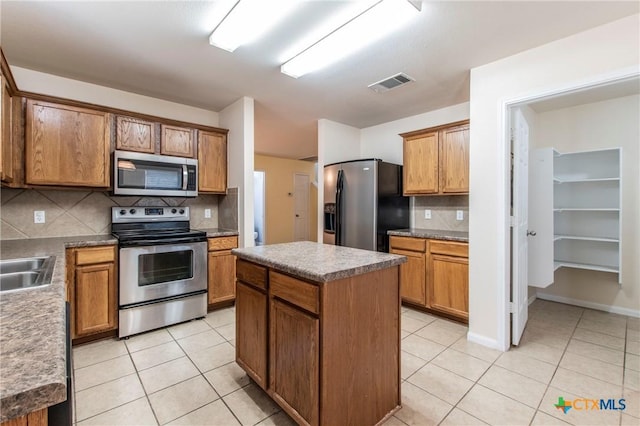 kitchen with sink, appliances with stainless steel finishes, a center island, light tile patterned flooring, and decorative backsplash