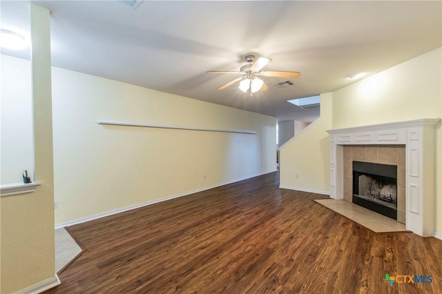 unfurnished living room with a tiled fireplace, dark wood-type flooring, and ceiling fan