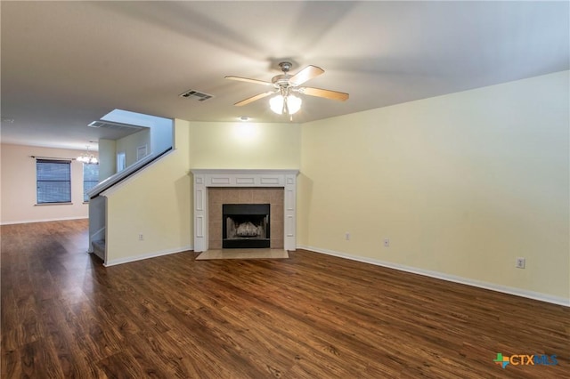 unfurnished living room featuring a tiled fireplace, ceiling fan with notable chandelier, and dark hardwood / wood-style flooring