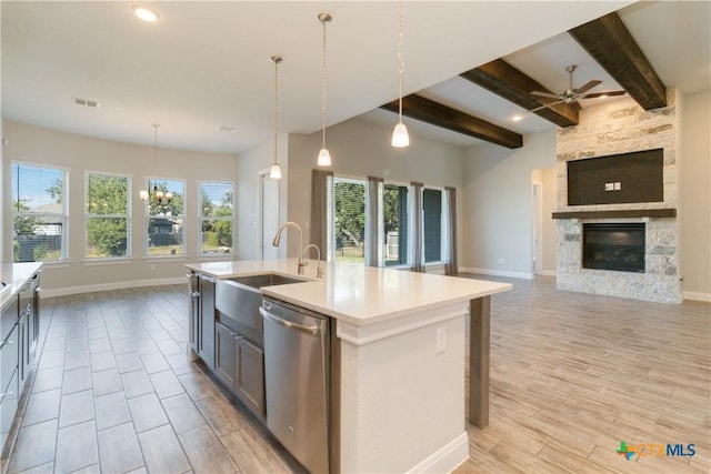 kitchen featuring a stone fireplace, an island with sink, stainless steel dishwasher, and decorative light fixtures