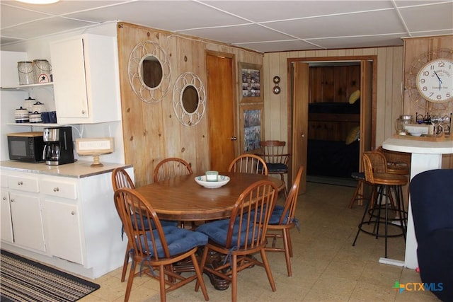 dining space with a paneled ceiling and wooden walls