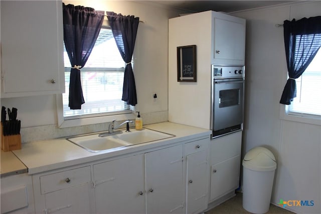 kitchen featuring white cabinets, sink, crown molding, and stainless steel oven