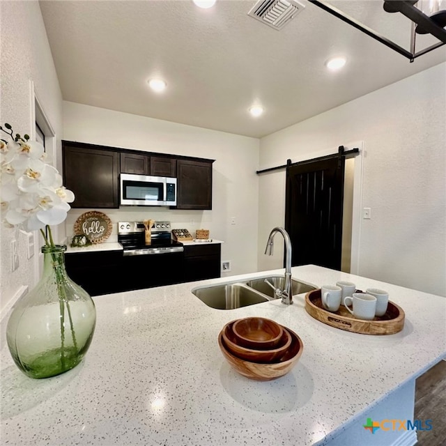 kitchen featuring sink, dark brown cabinets, light stone countertops, a barn door, and appliances with stainless steel finishes