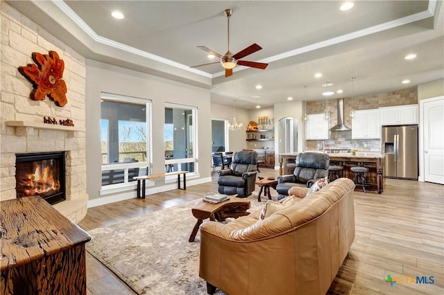 living area featuring a raised ceiling, a fireplace, and crown molding