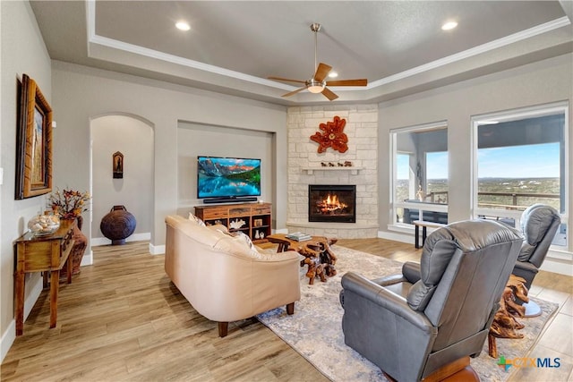 living area featuring a tray ceiling, crown molding, baseboards, and light wood-type flooring