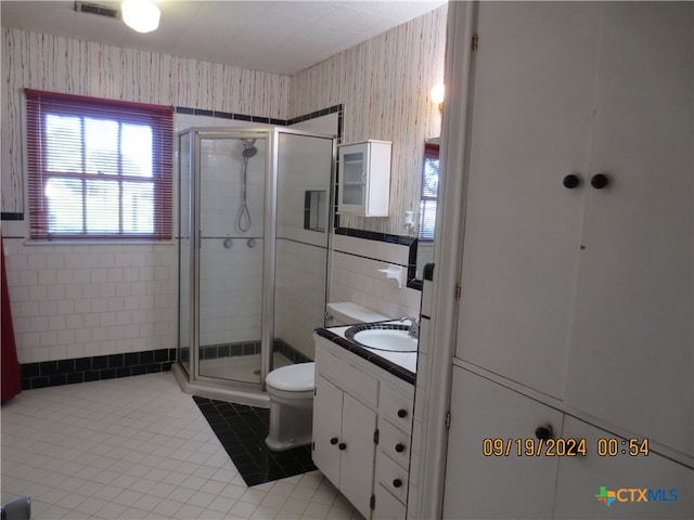 bathroom featuring walk in shower, tile patterned flooring, toilet, vanity, and tile walls