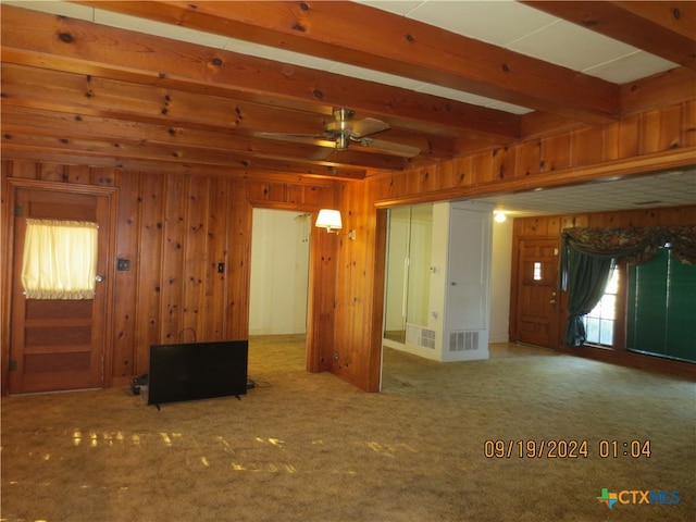 carpeted spare room with beamed ceiling, ceiling fan, and wood walls